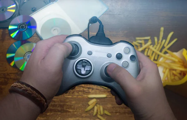 Eller, konsolun arka planındaki gri joystick 'i tutarken yere saçılmış diskler ve patatesler.