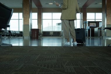 Havaalanı terminalinde elinde bavul tutan, ceketli, tanınmayan bir kadın.