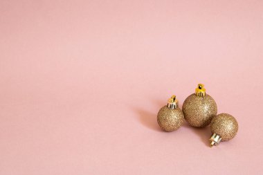 Pembe arka planda üç altın noel topunun yatay yakın çekimi..