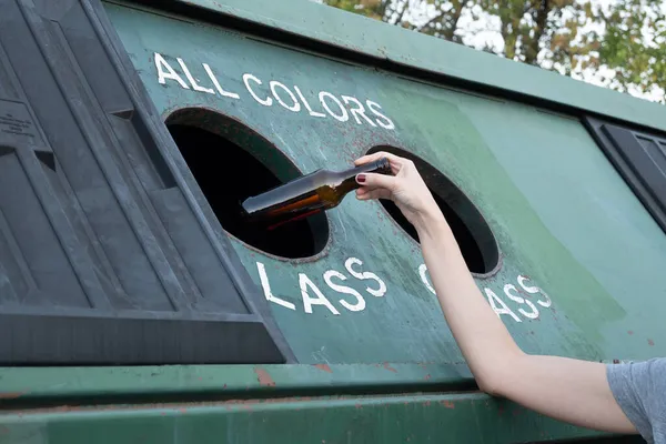 Close- up Unrecognizable woman pouring glass bottle into dumpster, with copy space