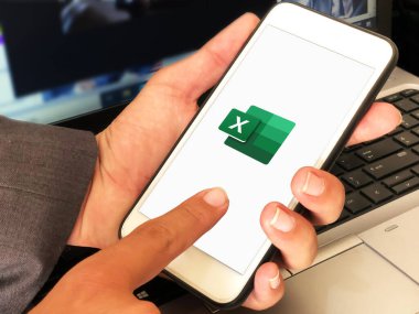 Mobil 'de Microsoft Excel kullanan adam. Arka planda dizüstü bilgisayar var. Mobil editörlük arka planında uzmanlık kullanan iş adamı