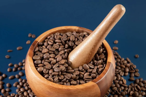 Ziarna kawy w drewnianej zaprawie. Ręczna młynek do kawy na niebieskim tle. Zbliżenie. — Zdjęcie stockowe