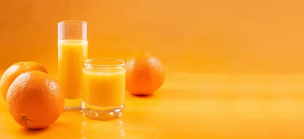 Orange juice in glasses and fresh oranges on an orange background. Banner. — Stock Photo, Image