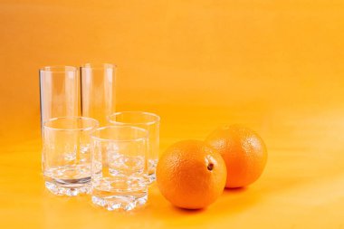 Turuncu arka planda boş bardaklar ve taze portakallar. Kavram.