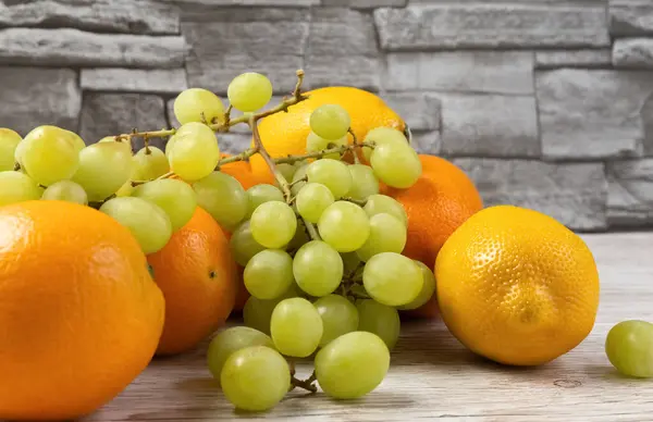 Čerstvé ovoce na stole. Pomeranče, citróny, hrozny na dřevěném stole. — Stock fotografie