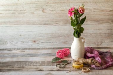 Beyaz bir vazoda bir buket çiçek, bir makas, bir ip ve ahşap zemin üzerinde bir mum. Kartpostal.