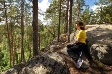 Dişi bir yürüyüşçü bir dağın tepesinde oturur ve manzaraya bakar. Fotoğraf.