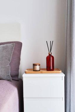 Yatak odasındaki komodinin üzerinde çubuk ve aroma mumu olan bir şişe parfüm yayıcı. İç tasarım ve ev dekorasyonu