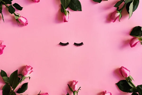 Sahte kirpikler ve pastel pembe arka planda gül çiçekleri. Güzellik konsepti. Kırbaç uzatma. Düz kadın yatağı, boşluğu kopyala