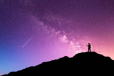 Samanyolu ile gece manzarası. Dağda kollarını kaldırmış genç bir adamın silueti. Güzel Evren. Seyahat arkaplanı 