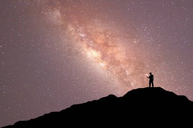Samanyolu ile gece manzarası. Dağda kollarını kaldırmış genç bir adamın silueti. Güzel Evren. Seyahat arkaplanı 