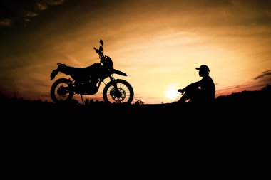Günbatımı arka planında motosikletle seyahat eden bir adamın siluetleri