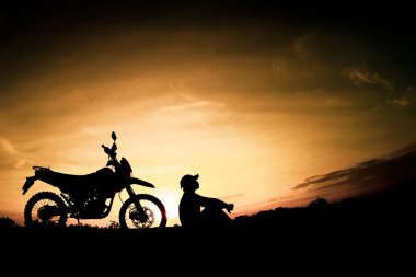 Günbatımı arka planında motosikletle seyahat eden bir adamın siluetleri