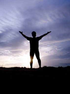Zevk ve özgürlük içinde elini kaldıran bir adamın silüeti. Akşamları ışık güzeldir.
