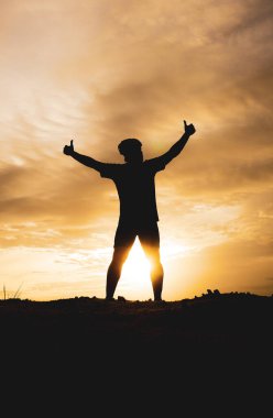 Zevk ve özgürlük içinde elini kaldıran bir adamın silüeti. Akşamları ışık güzeldir.