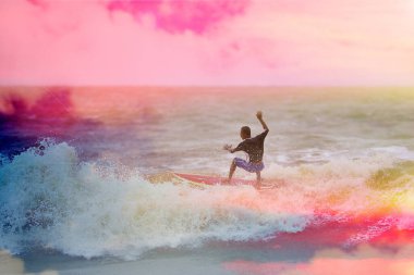 Sahilde dalgalarla sörf yapan.