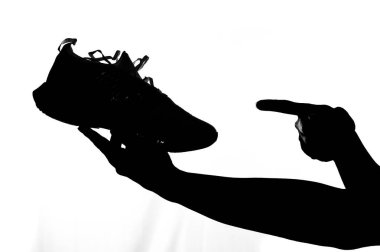 Beyaz arka planda koşan bir ayakkabıyı tutan bir adamın silueti. Koşu ayakkabısı almak ve egzersiz yapmak için fikirler.