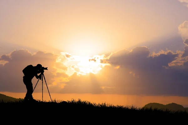 A professional photographer\'s silhouette is focused on shooting in a beautiful meadow.