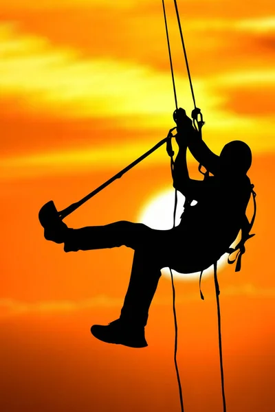 Silhouette of an adventurer climbing a rope on a high cliff in the evening. with clipping path