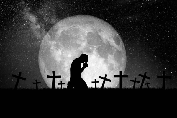 The idea of praying for peace to reduce the loss of war. A Christian man prays in a field with graves and moons.