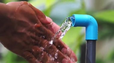 Su kaynakları kıtlığı kavramı. Adam musluğun altında ellerini yıkıyor ve su akıyor.