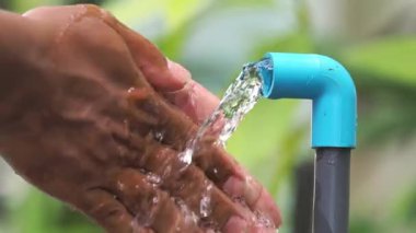 Su kaynakları kıtlığı kavramı. Adam musluğun altında ellerini yıkıyor ve su akıyor.