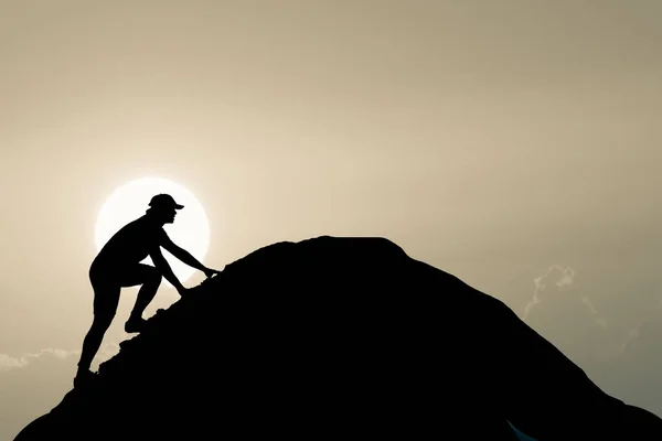 The man was climbing to the top of the mountain with a beautiful light effort. Silhouette of man climbing up steep edge of mountain. Fit young determined man climbing to top of mountain. People Never giving up, strength and power.