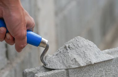 Endüstriyel tuğla ustasının elinde alüminyum mala havan topu var. İnşaat sahasında bir tuğla bloğa yerleştirilmiş ve metin için metin alanı seçici odak noktası var.                               