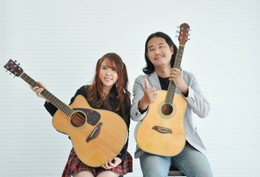 Gitarist, öğretmen ve elinde gitarlarla oturan bir öğrenci, öğretmen beyaz duvar arka planında izole edilmiş, akustik müzikal sınıfta.