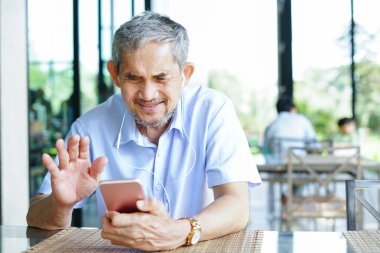 Restoran alanının dışında oturan Asyalı bir üst sınıf öğrencisi cep telefonuyla internetten birine el sallıyor ve konuşuyor. Yaşlılarda teknoloji kavramı                                                