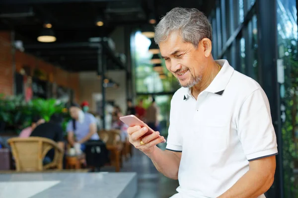 asian senior man smiling and using smartphone(selective focus at a man face),concept technology smartphone in elderly people for health care to improve memory,social interaction,doing business etc