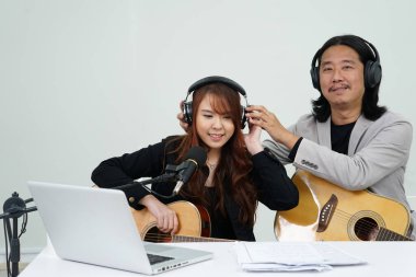 Baba-kız sanatçı konsepti stüdyoda dizüstü bilgisayardan canlı müzik, dizüstü bilgisayardan pratik yapan mutlu aile, dizüstü bilgisayardan müzik çalan aile.