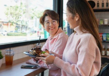 Romantik Igbtq lezbiyen aşığı tatlı pembe elbiseli kahve barında şekerleme ve içecek içen kapalı kafedeki cam pencere