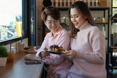 Romantik Igbtq lezbiyen aşığı tatlı pembe elbiseli kahve barında şekerleme ve içecek içen kapalı kafedeki cam pencere