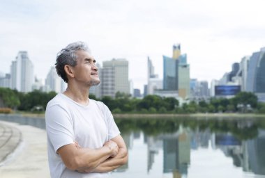 senior man with grey hair and beard standing and taking a deep breath after workout near the pond in nature atmosphere at the city park, concept for elderly people lifestyle,health care,well being,quality of life