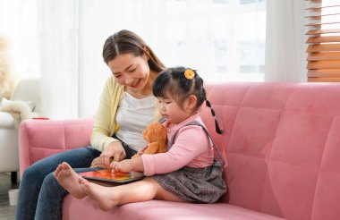 mother playing with her daughter   and using tablet in the living room