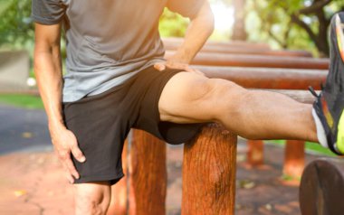 Antrenmandan önce bacak kasları ısınan bir erkek. Sağlıklı bir adam parkta egzersiz aletleri üzerinde bacaklarını esnetiyor.