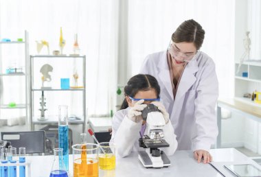 Bayan bilim adamı, öğrenciye laboratuarda fen eğitimi veriyor.