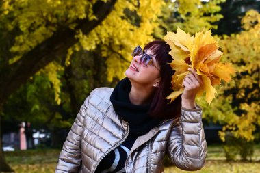 Çekici bir esmer, elinde bir buket sarı akçaağaç yaprağı tutuyor. Bayan sonbahar doğasını seviyor ve dikkatsizce gülümsüyor. Yakın plan portre