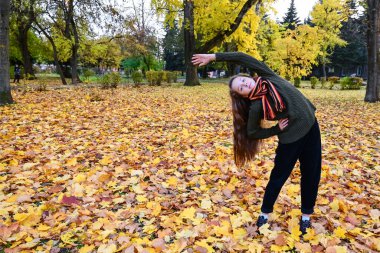 Güzel bir kız, sonbahar parkında, sarı yaprakların arasında egzersiz yapar, beden eğitimi, spor yapar, doğayı sever. Açık hava aktiviteleri