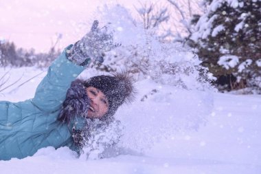 Mutlu bir kadın kışın tadını çıkarır, beyaz karı havaya fırlatır. Soğuk bir günde yürümek gibi. Sanatsal açıdan renkli ve renkli bir fotoğraf. Kış tatillerinde aktif dinlenme