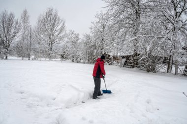 Kırmızı ceketli bir adam köyde kardan çıkan yolu kürekle temizliyor. Kış endişeleri