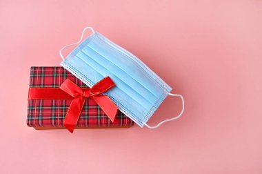 Tıbbi koruyucu maske pembe arka plandaki kırmızı hediye kutusunda yatıyor. Üst Manzara. Virüslerin bayram kutlamalarındaki etkisi. Boşluğu kopyala