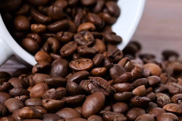 コーヒー豆は白いカップから木製のテーブルにこぼれ落ちる 木製の背景にコーヒー豆 — ストック写真