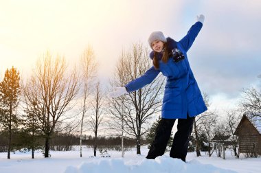 pretty girl in winter blue coat is standing outdoors on raised platform with her arms outstretched to sides. Girl stands against  background of blue sky with white clouds. Artistic toning. Copy space