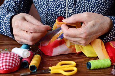 hands of an elderly woman with a sewing needle and a button. Seamstress's hands at work close-up. Employment of  elderly