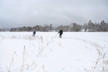 Sırt çantalı turistler donmuş bir nehirde kayak yapmaya giderler. Karla kaplı ağaçlarla kaplı kış manzarası.