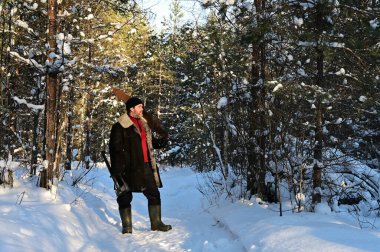 Sakallı ve düğmesiz kuzu derisi ceketli vahşi bir adam karla kaplı bir ormanın ortasında duruyor. Adam bir balta ve el testeresi tutuyor. Güneşli kış günü. Yakacak odun topluyorum.