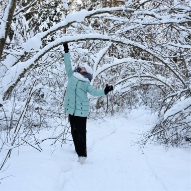 pretty stylish girl walks in winter park among trees covered with snow. Girl is wearing warm jacket, white hat and scarf. Comfortable clothes for walking in winter