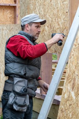 Elinde elektrikli tornavidayla inşaatçının portresi. Erkek işçi tornavidayla ahşap yapı inşa eder. Endüstriyel konu. İnşaat şirketinde çalışıyorum.